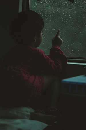 A child runs his finger along the wet glass on the train