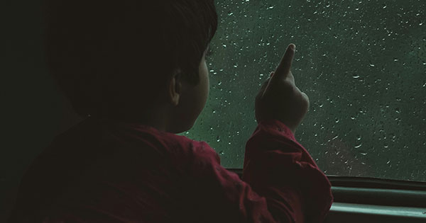 A child runs his finger along the wet glass on the train